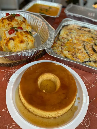 Foil trays of hot baked dishes alongside a whole flan