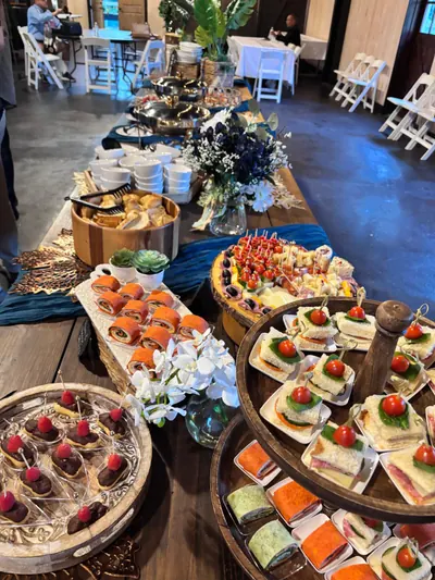 Long reception buffet of canapés, desserts and flowers in a venue set with white chairs