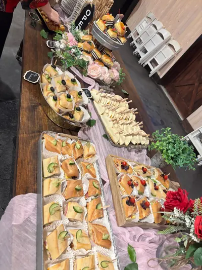 Long table of cucumber canapés, pastries and cheese trays dressed with roses